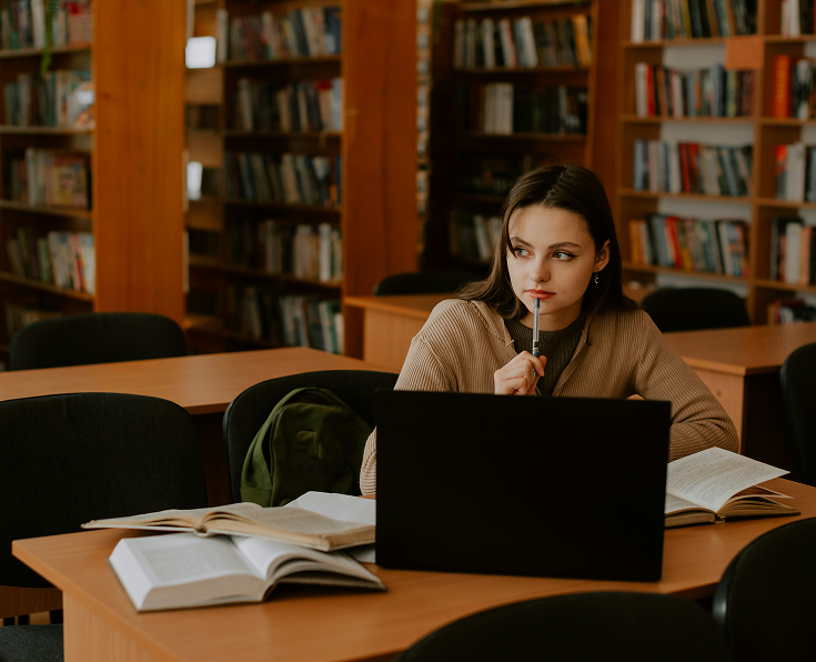 Elev studerar vid en laptop i ett bibliotek med böcker bakom