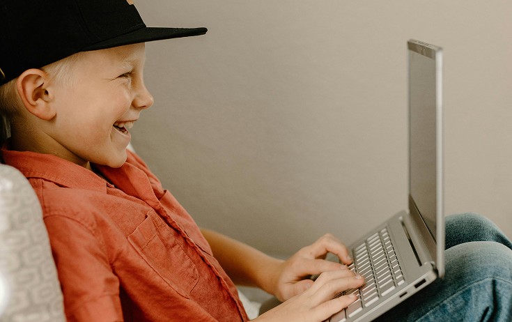 Yngre elev med svart keps studerar leende vid sin laptop